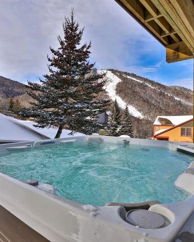 Indoor hot tub with water jets in a room with wood finishes and large windows with forest views.