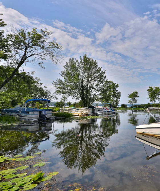 Wide-angle view of Lake Bomoseen in Vermont, with a boat, a boat ramp, a clear sky, and large trees around the lake.