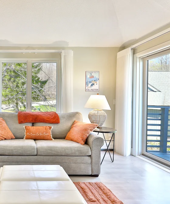 Interior of a vacation condo with large windows and a sofa. Decorated in pastel colors. Trees seen outside.