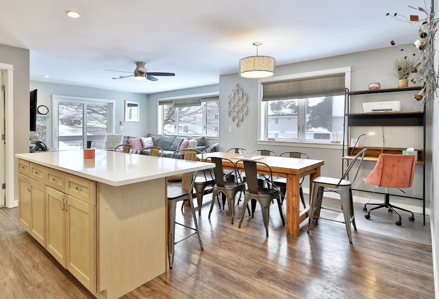 Open-concept living space of a vacation condo in Killington, with a kitchen island with bar stools, a dining table, and large windows with mountain views.