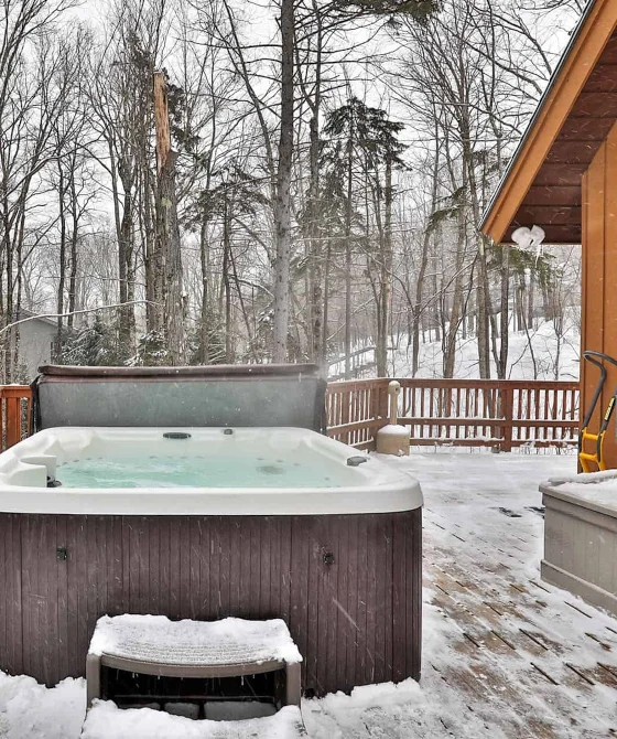 Hot tub at a large deck of a vacation-rental home in Killington during the winter. A snowy landscape with birch trees is seen in the background.