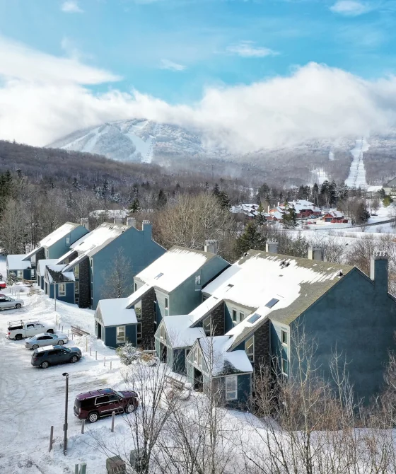 Aerial winter view of the different buildings that make the Whiffletree Condos complex next to Killington Mountain. Cars parked in front of them.