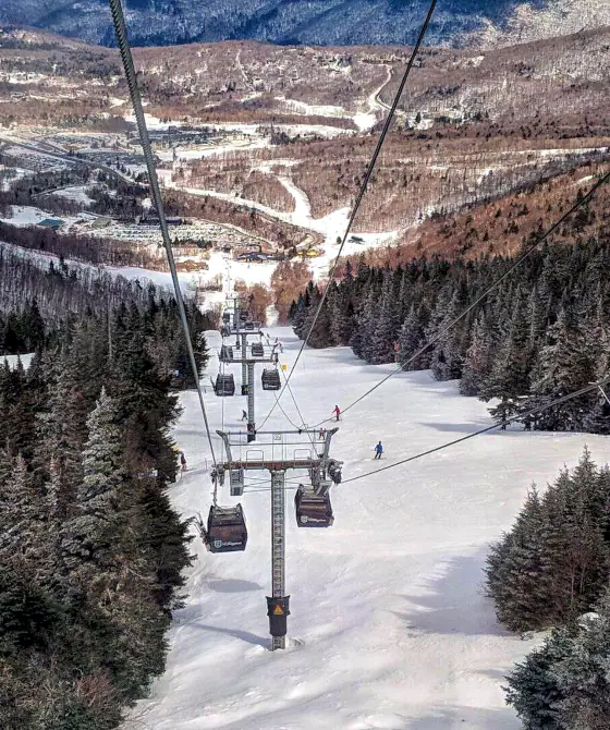 Winter aerial view of lifts at Pico Mountain, Vermont, surrounded by trees.