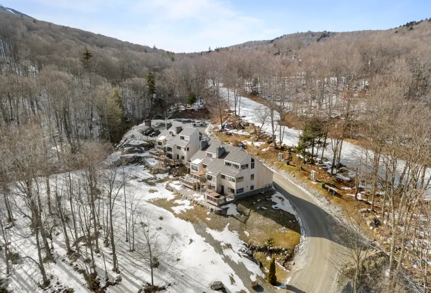 Drone view of the buildings that make Trailside Village in Killington, next to a road, forests around, mountains nearby, in the Vermont winter.