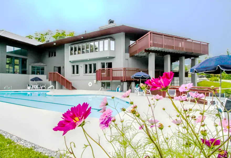 Outdoor pool surrounded by lawn with flowers, and a large building nearby.