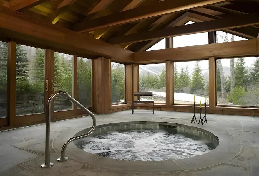 Round hot tub with water jets, set in a room surrounded by wide windows overlooking the forest.