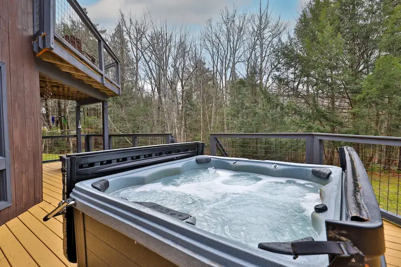 Deck of a Vermont vacation cabin with a hot tub and a view of the Vermont forest.
