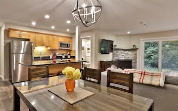 Stylish dining area and open kitchen in a vacation condo with a fireplace in the background.